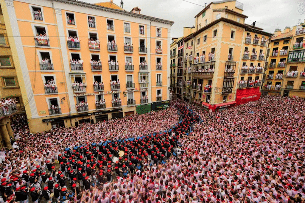 Inside the Running of the Bulls: A Complete Cultural Guide to Pamplona’s San Fermín Festival photo | Cosmopolitours Aerial view of a dense crowd dressed in white and red celebrating the opening ceremony of the San Fermín Festival in Pamplona, Spain.