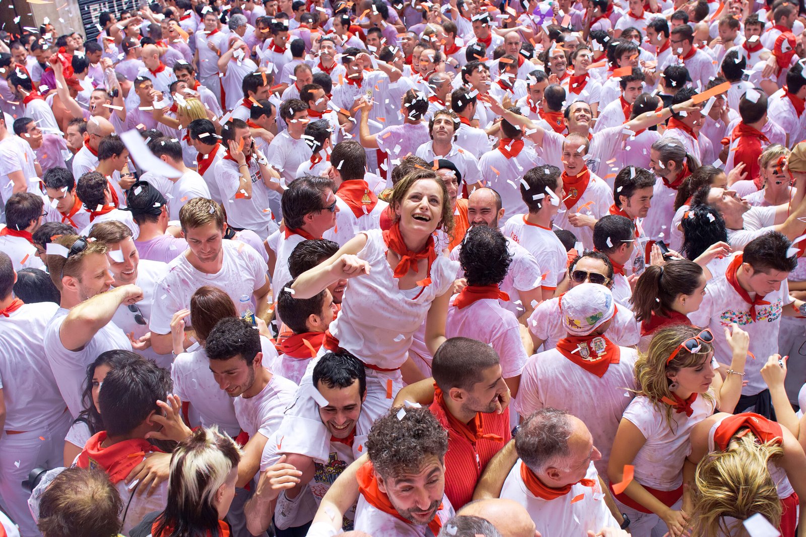 Crowd of San Fermín festival-goers in traditional white and red attire celebrating with confetti in Pamplona, Spain