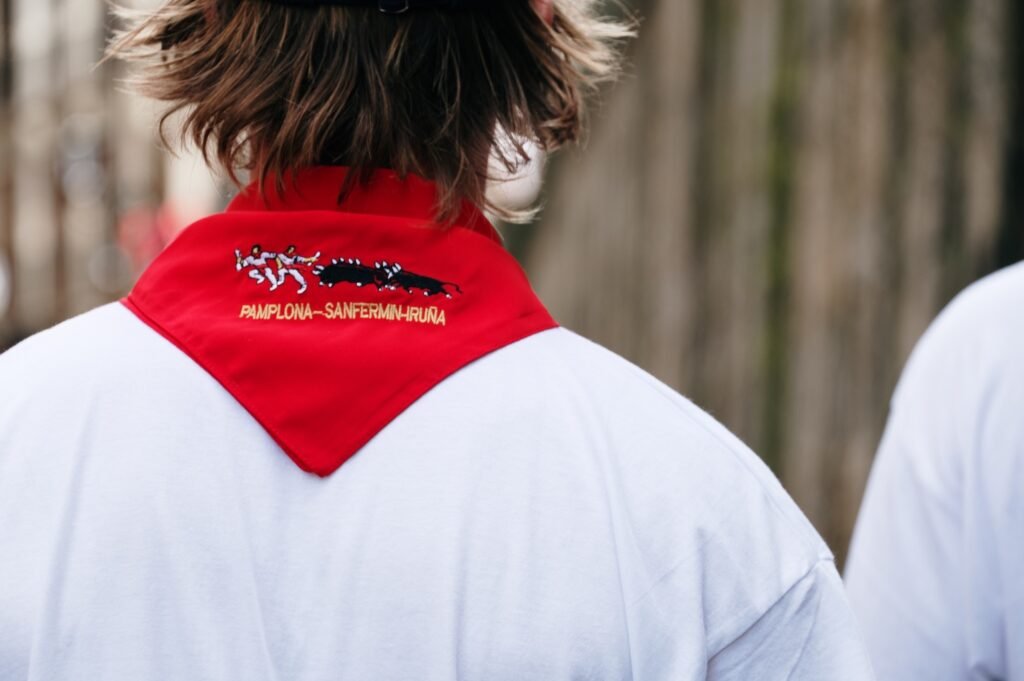 Inside the Running of the Bulls: A Complete Cultural Guide to Pamplona’s San Fermín Festival photo | Cosmopolitours Close-up of the traditional red scarf, or pañuelo, worn during the San Fermín Festival in Pamplona, embroidered with runners and bulls and the words “Pamplona – Sanfermin – Iruña.”