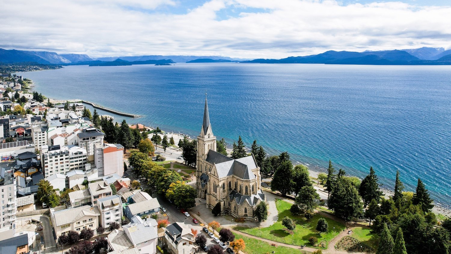 Cooler Summer Destinations in South America: The Coolcation the World Forgot photo | Cosmopolitours Bariloche, Argentina, with the cathedral and Lake Nahuel Huapi framed by the Andes mountains, showcasing Patagonia as a serene luxury coolcation destination.