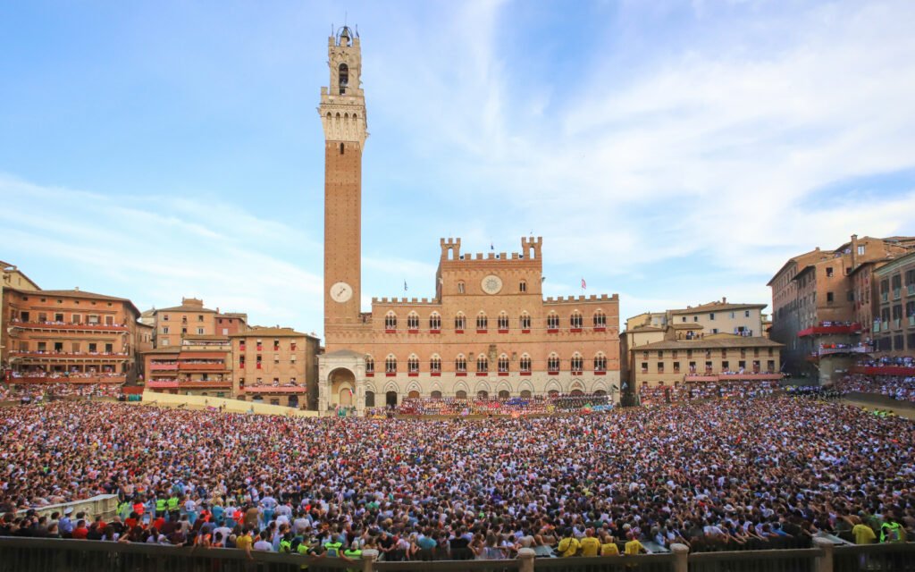 Piazza del Campo in Siena filled with thousands of spectators gathered to watch the Palio di Siena horse race in front of the Palazzo Pubblico.