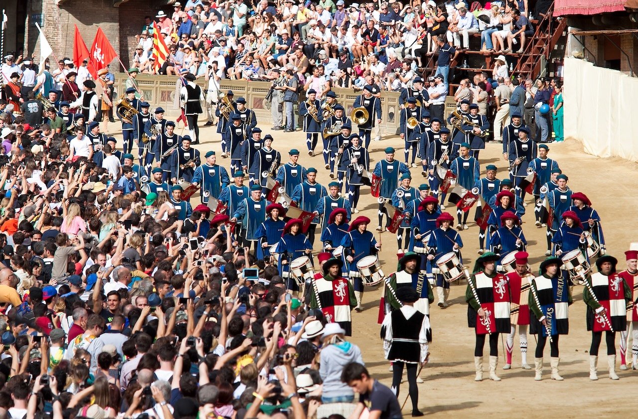 The Corteo Storico procession in Piazza del Campo during the Palio di Siena, featuring drummers, flag bearers, and performers in Renaissance costumes.